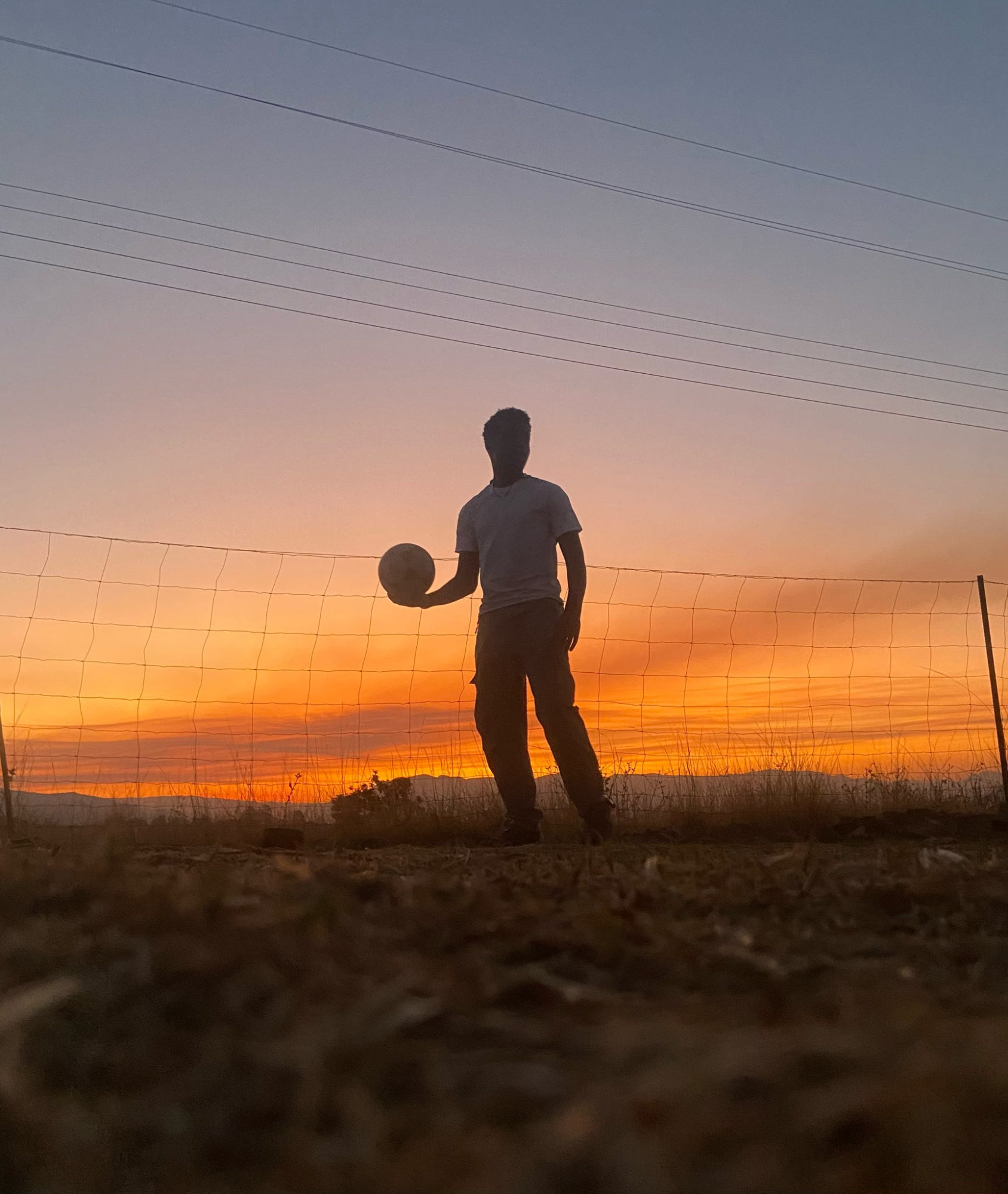 Student holding football against orange sunset in Eswatini